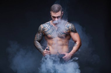 Vaper. Dövmeli bir kaslı çıplak gövde adamla koyu arka plan üzerinde elektronik sigara duman