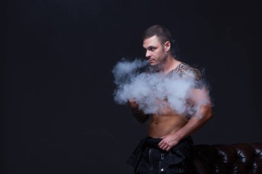 Vaper. Dövmeli bir kaslı çıplak gövde adamla koyu arka plan üzerinde elektronik sigara duman
