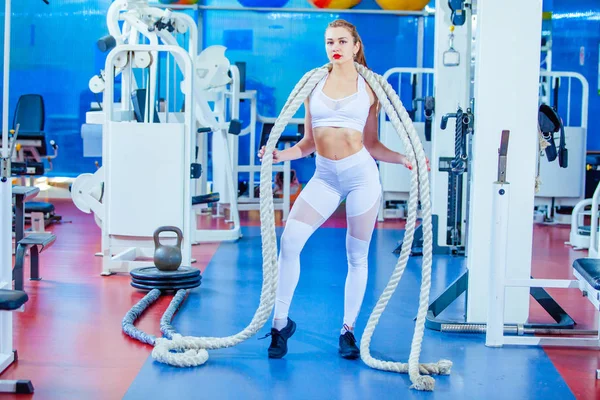 Donna fitness che si allena con corda da battaglia in palestra. posa sulla macchina fotografica — Foto Stock