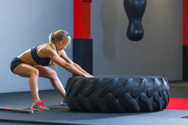 Apto atleta feminino exercitando-se com um pneu enorme, puxa no ginásio. Crossfit mulher exercitando com pneu grande — Fotografia de Stock