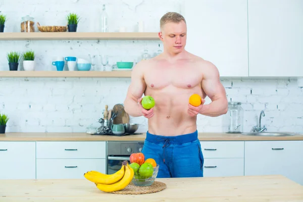 Homem musculoso com um tronco nu na cozinha com frutas, conceito de alimentação saudável. Modo de vida atlético . — Fotografia de Stock