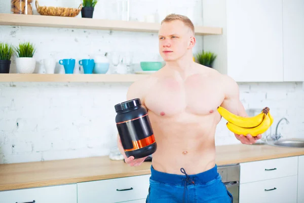 Svalnatý muž nahý trup v kuchyni s sportovní výživy proteiny a banány, koncept zdravé stravy. Sportovní způsob života. — Stock fotografie