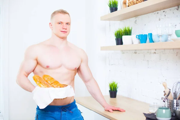 Homem musculoso com um tronco nu na cozinha com pão, conceito de alimentação saudável. Modo de vida atlético . — Fotografia de Stock