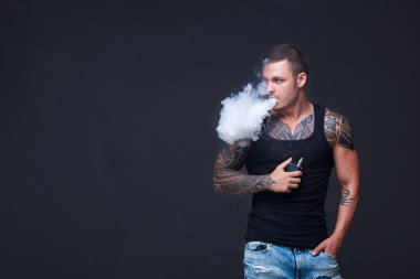 Vaper. Dövmeli kas bir gövde adamla koyu arka plan üzerinde elektronik sigara duman