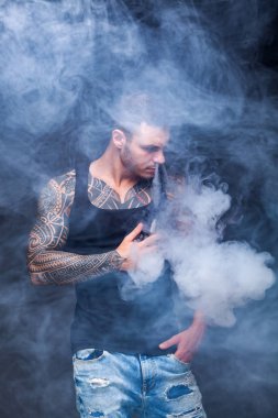 Vaper. Dövmeli kas bir gövde adamla koyu arka plan üzerinde elektronik sigara duman