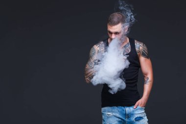 Vaper. Dövmeli kas bir gövde adamla koyu arka plan üzerinde elektronik sigara duman