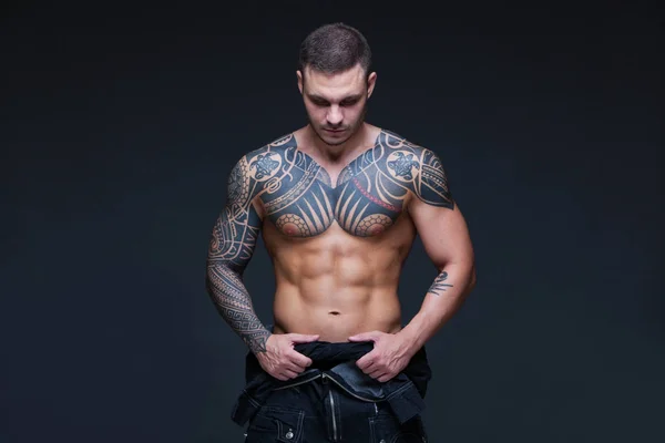 El hombre con un torso desnudo muscular con tatuajes en el fondo oscuro. ABS —  Fotos de Stock