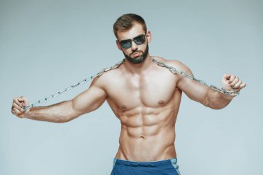.vücut geliştirmeci poz. Güzel sportif adam erkek güç. Fitness mavi şort ve güneş gözlüğü kaslı. izole gri arka plan üzerinde. Kas gövde olan adam. Güçlü atletik erkek Fitness modeli gövde