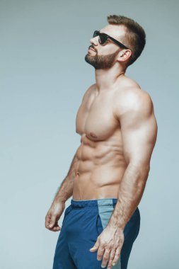 .vücut geliştirmeci poz. Güzel sportif adam erkek güç. Fitness mavi şort ve güneş gözlüğü kaslı. izole gri arka plan üzerinde. Kas gövde olan adam. Güçlü atletik erkek Fitness modeli gövde