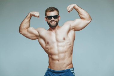 .vücut geliştirmeci poz. Güzel sportif adam erkek güç. Fitness mavi şort ve güneş gözlüğü kaslı. izole gri arka plan üzerinde. Kas gövde olan adam. Güçlü atletik erkek Fitness modeli gövde