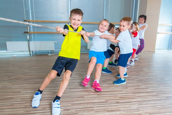 Anak-anak dan rekreasi, sekelompok anak sekolah multietnis yang bahagia bermain tarik-menarik perang dengan tali di gym — Stok Foto