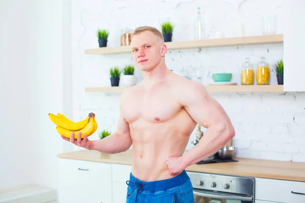 Muscular man with a naked torso in the kitchen with fruit, concept of healthy eating. Athletic way of life. — Stock Photo, Image