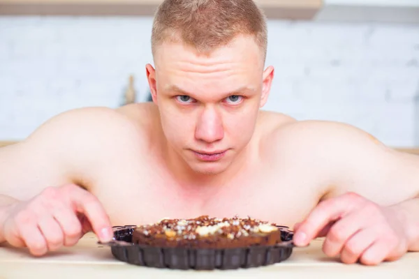 Homem musculoso com um tronco nu na cozinha com torta, o conceito de uma dieta saudável. Estilo de vida atlético. A tentação de doce . — Fotografia de Stock