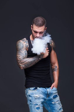 Vaper. Dövmeli kas bir gövde adamla koyu arka plan üzerinde elektronik sigara duman