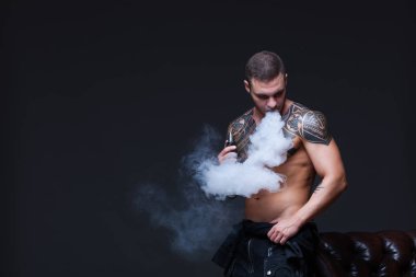 Vaper. Dövmeli bir kaslı çıplak gövde adamla koyu arka plan üzerinde elektronik sigara duman