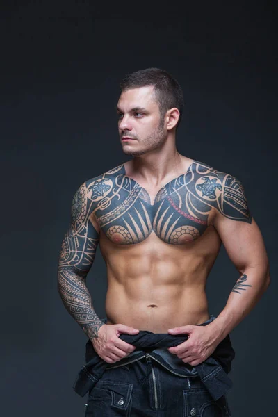 El hombre con un torso desnudo muscular con tatuajes en el fondo oscuro. ABS —  Fotos de Stock