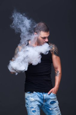 Vaper. Dövmeli kas bir gövde adamla koyu arka plan üzerinde elektronik sigara duman