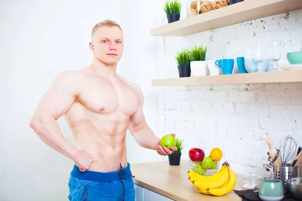 Muscular man with a bare torso in the kitchen with an apple and bananas, the concept of a healthy diet. Athletic way of life. — Stock Photo, Image