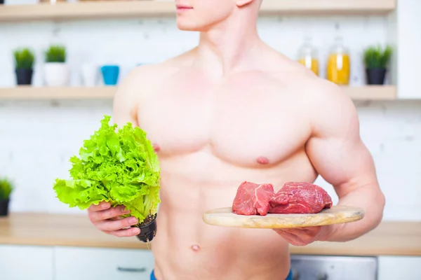 肌肉发达的男人带着一个赤裸的躯干在厨房里配上沙拉和一块牛肉肉, 健康饮食的概念。运动的生活方式. — 图库照片