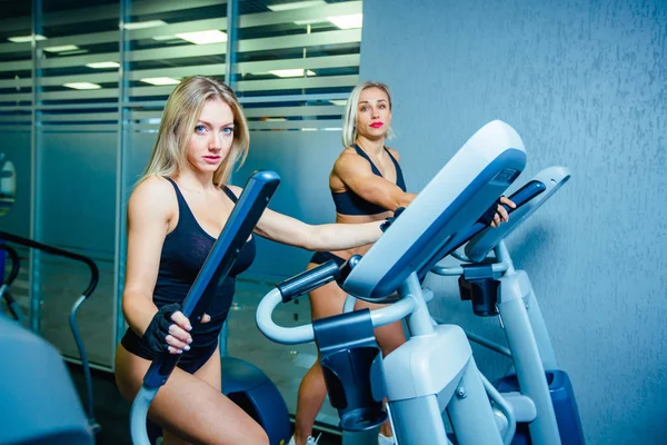 Positif deux amies s'entraînant sur des entraîneurs elliptiques dans un club de fitness, concept de style de vie. entraînement cardio, combustion des graisses, perte de poids — Photo