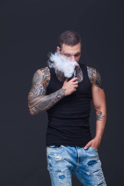 Vaper. Dövmeli kas bir gövde adamla koyu arka plan üzerinde elektronik sigara duman