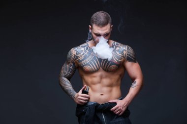 Vaper. Dövmeli bir kaslı çıplak gövde adamla koyu arka plan üzerinde elektronik sigara duman