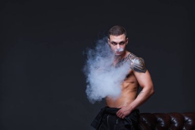 Vaper. Dövmeli bir kaslı çıplak gövde adamla koyu arka plan üzerinde elektronik sigara duman
