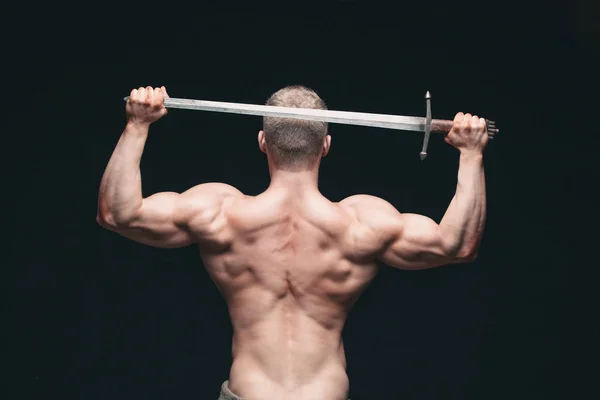 Bodybuilder man poseren met een zwaard geïsoleerd op zwarte achtergrond. Ernstige shirtless man aan te tonen zijn mascular lichaam. zwaard voor hoofd — Stockfoto