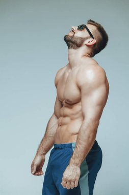 .vücut geliştirmeci poz. Güzel sportif adam erkek güç. Fitness mavi şort ve güneş gözlüğü kaslı. izole gri arka plan üzerinde. Kas gövde olan adam. Güçlü atletik erkek Fitness modeli gövde