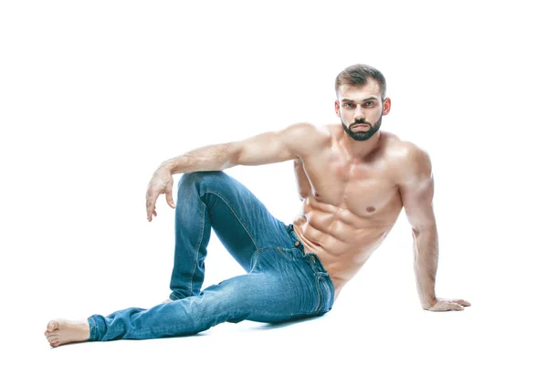 Fisiculturista posando. Bonito desportista poder masculino. Fitness musculado em jeans azuis. sobre fundo branco isolado. senta-se no chão — Fotografia de Stock