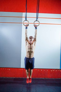 Jimnastik halkaları üzerinde spor salonunda egzersiz kas-up egzersiz yoğun yapan genç erkek çapraz yerleştirmek.