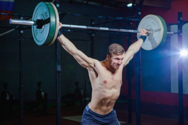 Yakışıklı bir atlet portresi. Atlet halter başının üzerine yükseltir. çekim koyu tonda. Çapraz tarzı uygun, deadlift