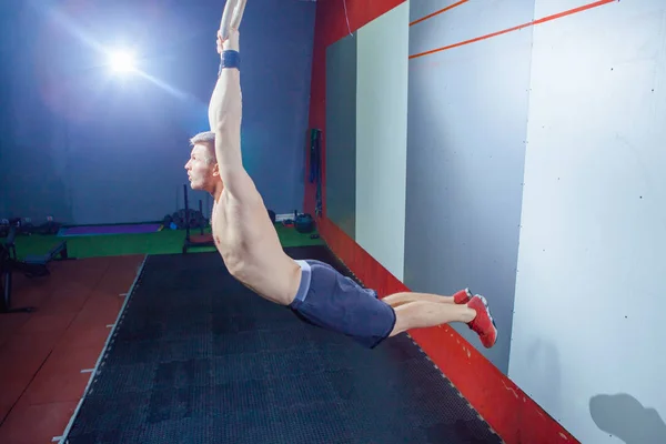 Muscle-up motion ung man gör intensiv cross fit träning på gymmet på Gymnastringar. — Stockfoto