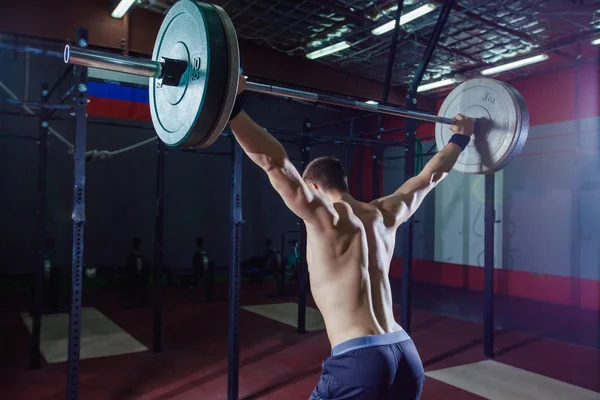 Arkadan bir yakışıklı sporcu portresi. Atlet halter başının üzerine yükseltir. Stüdyo çekim koyu tonda. Çapraz tarzı uygun, deadlift