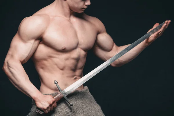 Bodybuilder man posing with a sword isolated on black background. Serious shirtless man demonstrating his mascular body — Stock Photo, Image