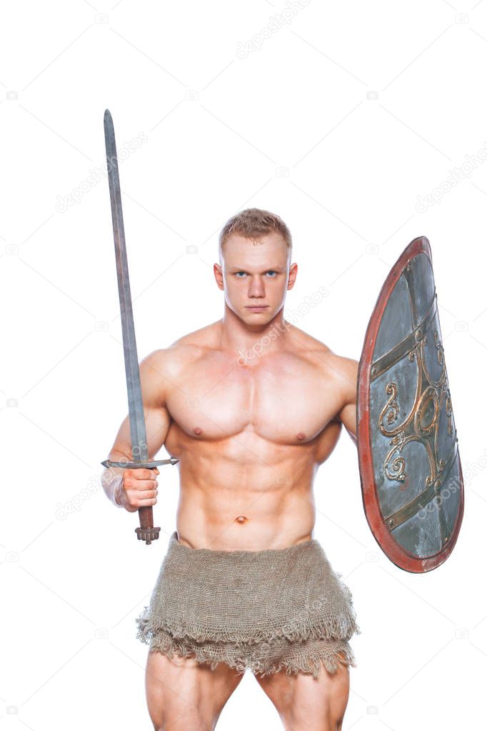 Bodybuilder man posing with a sword and shield isolated on white background. Serious shirtless man demonstrating his mascular body.