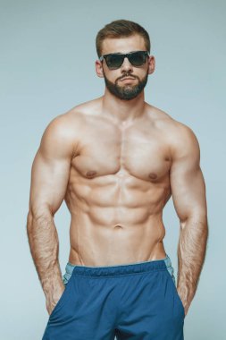 .vücut geliştirmeci poz. Güzel sportif adam erkek güç. Fitness mavi şort ve güneş gözlüğü kaslı. izole gri arka plan üzerinde. Kas gövde olan adam. Güçlü atletik erkek Fitness modeli gövde