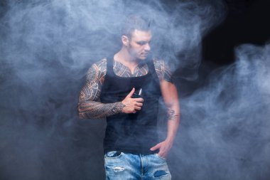 Vaper. Dövmeli kas bir gövde adamla koyu arka plan üzerinde elektronik sigara duman