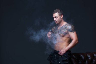 Vaper. Dövmeli bir kaslı çıplak gövde adamla koyu arka plan üzerinde elektronik sigara duman