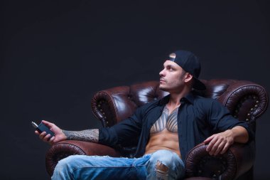 Vaper. Dövmeli adam koyu arka plan üzerinde elektronik sigara duman deri kanepede oturuyor.