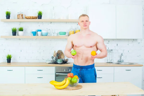 Homem musculoso com um tronco nu na cozinha com frutas, conceito de alimentação saudável. Modo de vida atlético . — Fotografia de Stock