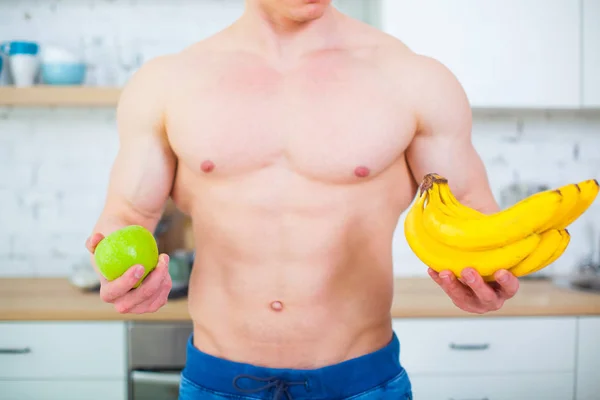 Homem musculoso com um tronco nu na cozinha com frutas, conceito de alimentação saudável. Estilo de vida atlético. Bananas close-up . — Fotografia de Stock