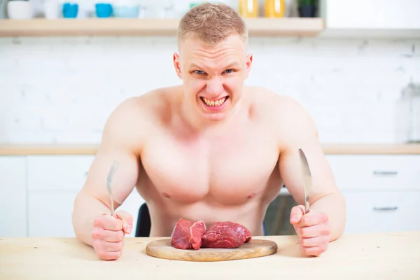 Hombre musculoso con un torso desnudo en la cocina con un trozo de carne de res, el concepto de una dieta saludable. Estilo de vida atlético . — Foto de Stock