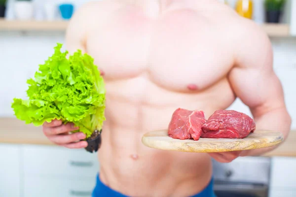 Muskulös man med en naken torso i köket med en sallad och en bit nötkött kött, begreppet en hälsosam kost. Atletisk livsföring. — Stockfoto