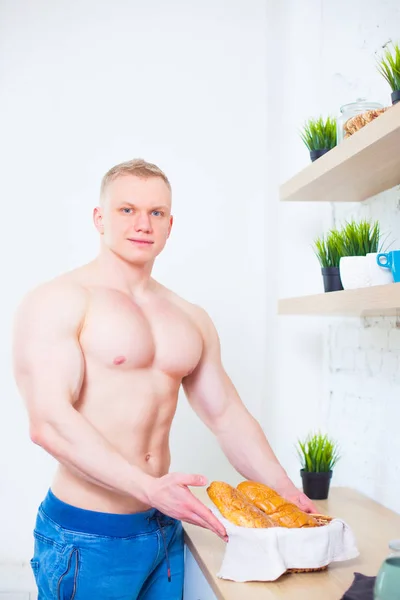 Hombre musculoso con un torso desnudo en la cocina con pan, concepto de alimentación saludable. Estilo de vida atlético . — Foto de Stock
