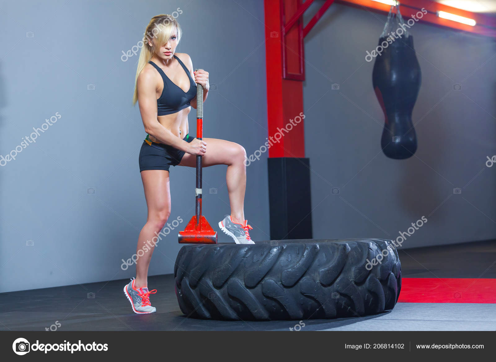 Fitness woman hitting wheel tire with hammer sledge in the gym. Stock