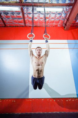 Jimnastik halkaları üzerinde spor salonunda egzersiz kas-up egzersiz yoğun yapan genç erkek çapraz yerleştirmek.
