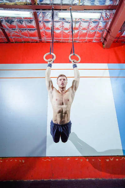 Muscle-up exercise young man doing intense cross fit workout at the gym on gymnastic rings.