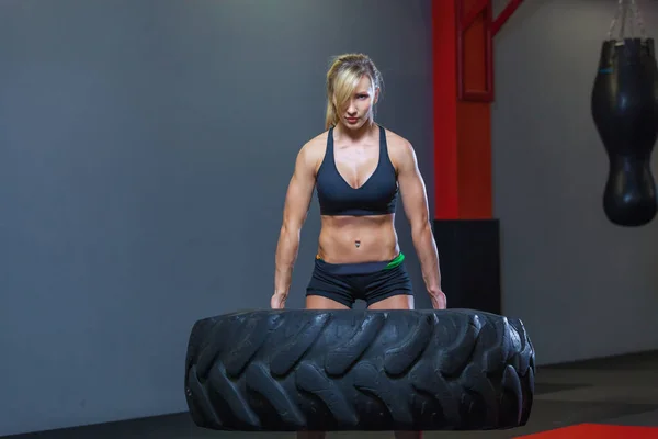 Apto atleta feminino exercitar-se com um pneu enorme, girando e transportar no ginásio. Crossfit mulher exercitando com pneu grande — Fotografia de Stock