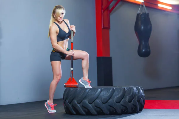 Fitness woman hitting wheel tire with hammer sledge in the gym.